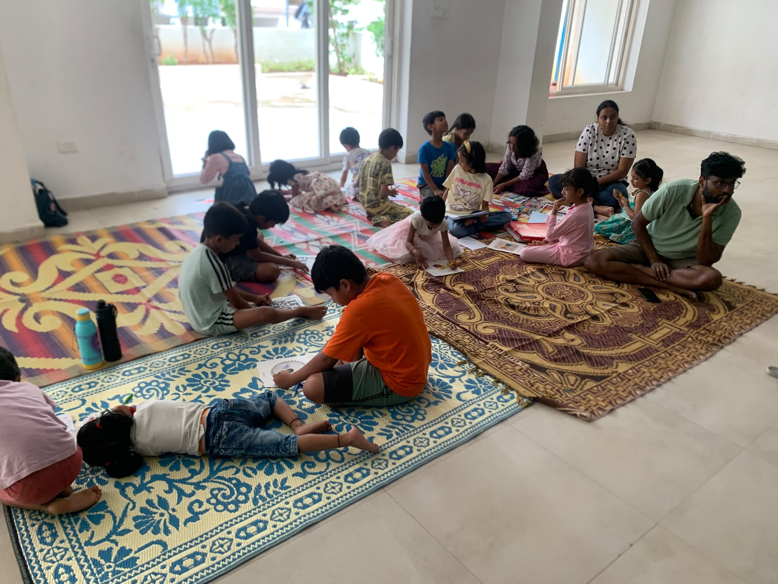 Children sitting on colourful mats colouring together while a parent and facilitator watch