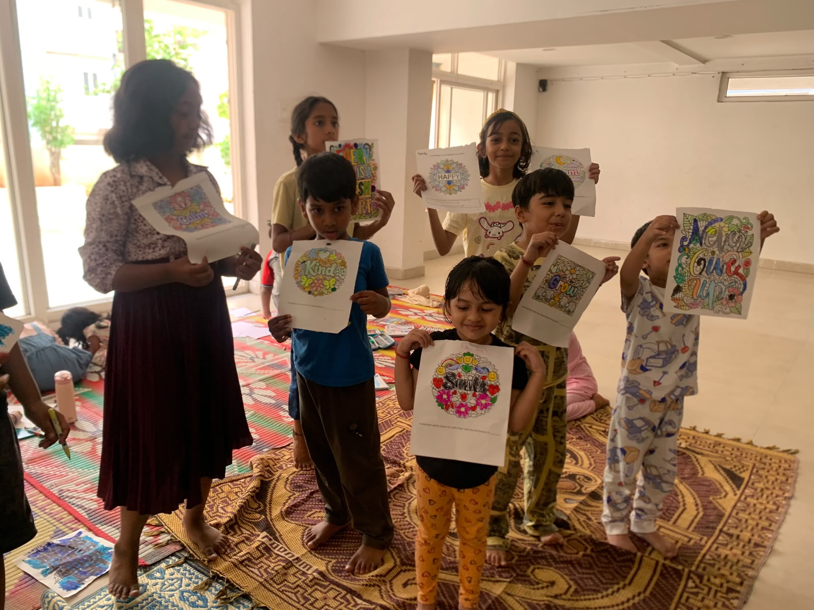 A group of children standing together holding up finished mindfulness art with their facilitator