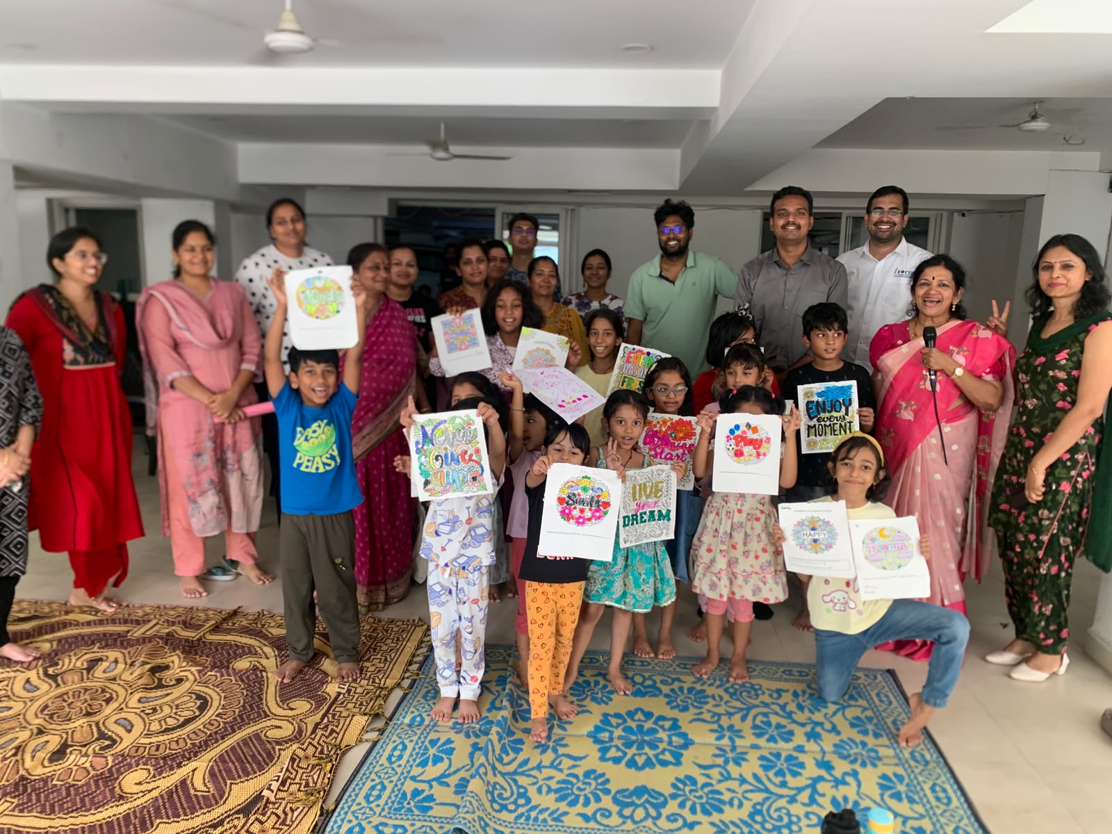 Children, parents and Jignyasa facilitators together at a well-being session, holding up their colourful artwork